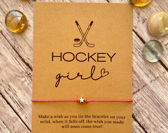 May include: A brown card with a hockey stick and puck graphic and the text "HOCKEY girl" with a heart. The card is attached to a pink string bracelet with a silver star charm. The text on the card reads "Make a wish as you tie the bracelet on your wrist, when it falls off, the wish you made will soon come true!"