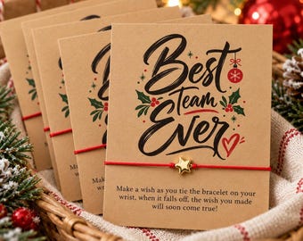 May include: A stack of kraft paper cards featuring the text Best Team Ever in black script, decorated with red and green holly and a red ornament. Each card holds a red string bracelet with a small gold star charm and printed instructions.