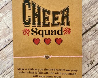 May include: A pink friendship bracelet with a silver heart charm. The card reads "CHEER *Squad*" with three red hearts and the text "Make a wish as you tie the bracelet on your wrist, when it falls off, the wish you made will soon come true!"