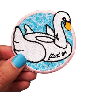 May include: White embroidered patch of a swan floating on blue water with the text "float on" in black.
