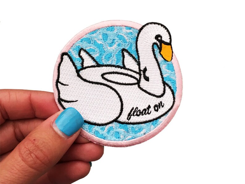 May include: White embroidered patch of a swan floating on blue water with the text "float on" in black.