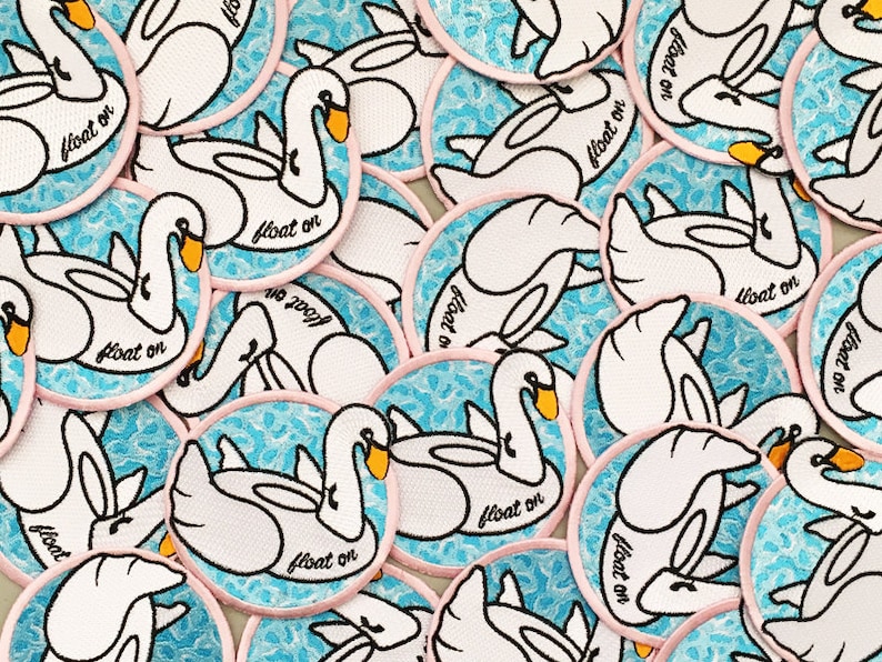May include: A collection of embroidered iron-on patches featuring white swans on a blue and white water pattern. Each patch has a pink border and the text "float on" in black.