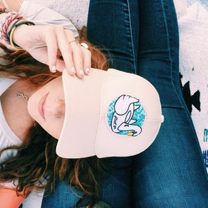 May include: A pink baseball cap with a white swan graphic and the text "float on" in blue. The swan is holding a yellow object in its beak.
