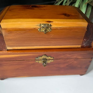 May include: Two wooden boxes with brass hinges and latches. The top box is a lighter shade of wood and has a more ornate latch. The bottom box is a darker shade of wood and has a simpler latch.