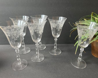 May include: Set of six clear glass wine glasses with an etched floral design. The glasses have a tall, slender stem and a bowl that flares out at the top.