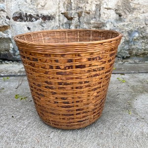 May include: A woven wicker basket with a brown and tan color scheme. The basket is round and has a wide opening.