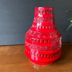 May include: A red ceramic vase with a geometric pattern. The vase has a wide base and a narrow neck.