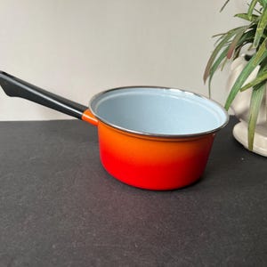 May include: A small, vintage saucepan with a black handle and a vibrant gradient of orange to red enamel. The interior is light blue, and the rim is silver. A classic kitchenware item.