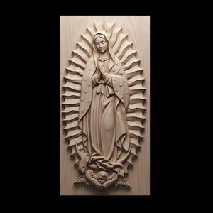 Puede incluir: Un relieve de madera de la Virgen María, representada con una túnica fluida y un halo de luz. El tallado es detallado, con pliegues visibles en la tela y rasgos faciales intrincados. La obra de arte está montada sobre un panel de madera rectangular.