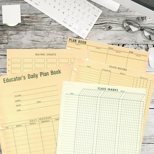 Puede incluir: Un conjunto de páginas de planificador de profesor amarillo y verde con encabezados para diagramas de asientos, programa diario, registro de clase y calificaciones de clase. Las páginas están sobre una mesa de madera con un teclado, gafas y un ratón blanco.