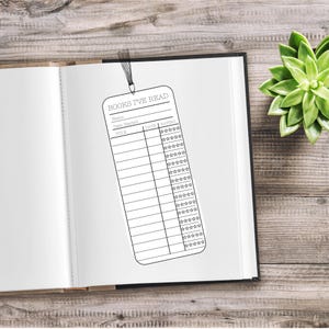 May include: A black and white bookmark with the text "BOOKS I'VE READ" and sections for title, date started, and rating. The bookmark is inside an open book on a wooden surface.