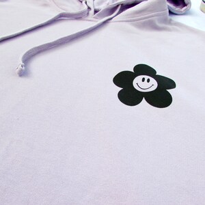 May include: A lavender hoodie with a black flower graphic featuring a white smiley face.