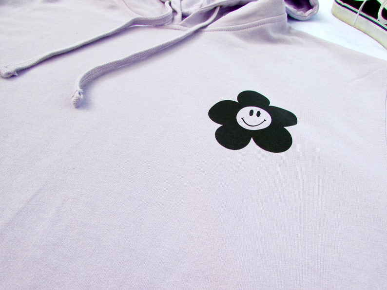 May include: A lavender hoodie with a black flower graphic featuring a white smiley face.