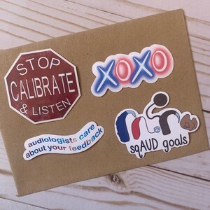 Op de afbeelding: Een set van vijf stickers met verschillende ontwerpen. E&eacute;n sticker is een rood stopteken met de tekst "STOP CALIBRATE & LISTEN". Een andere sticker is een blauw en rood ontwerp met de tekst "audiologists care about your feedback". Een derde sticker is een blauw en rood ontwerp met de tekst "XOXO". Een vierde sticker is een blauw, rood en wit ontwerp met de tekst "SQUAD goals" en een gestileerde afbeelding van een hoortoestel.