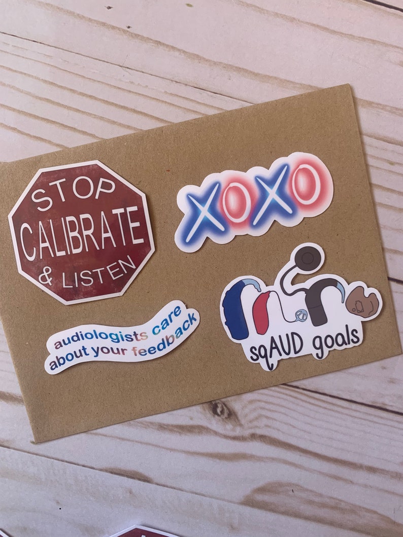 Op de afbeelding: Een set van vijf stickers met verschillende ontwerpen. E&eacute;n sticker is een rood stopteken met de tekst "STOP CALIBRATE & LISTEN". Een andere sticker is een blauw en rood ontwerp met de tekst "audiologists care about your feedback". Een derde sticker is een blauw en rood ontwerp met de tekst "XOXO". Een vierde sticker is een blauw, rood en wit ontwerp met de tekst "SQUAD goals" en een gestileerde afbeelding van een hoortoestel.
