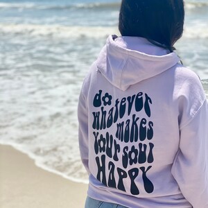 May include: A lavender hoodie with the text "do whatever makes your soul happy" in a retro font on the back.