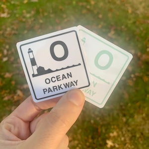 May include: Two stickers with a lighthouse and the text "Ocean Parkway" and the letter "O" in black and white. The sticker on top is white with black text and the sticker on the bottom is green with white text.
