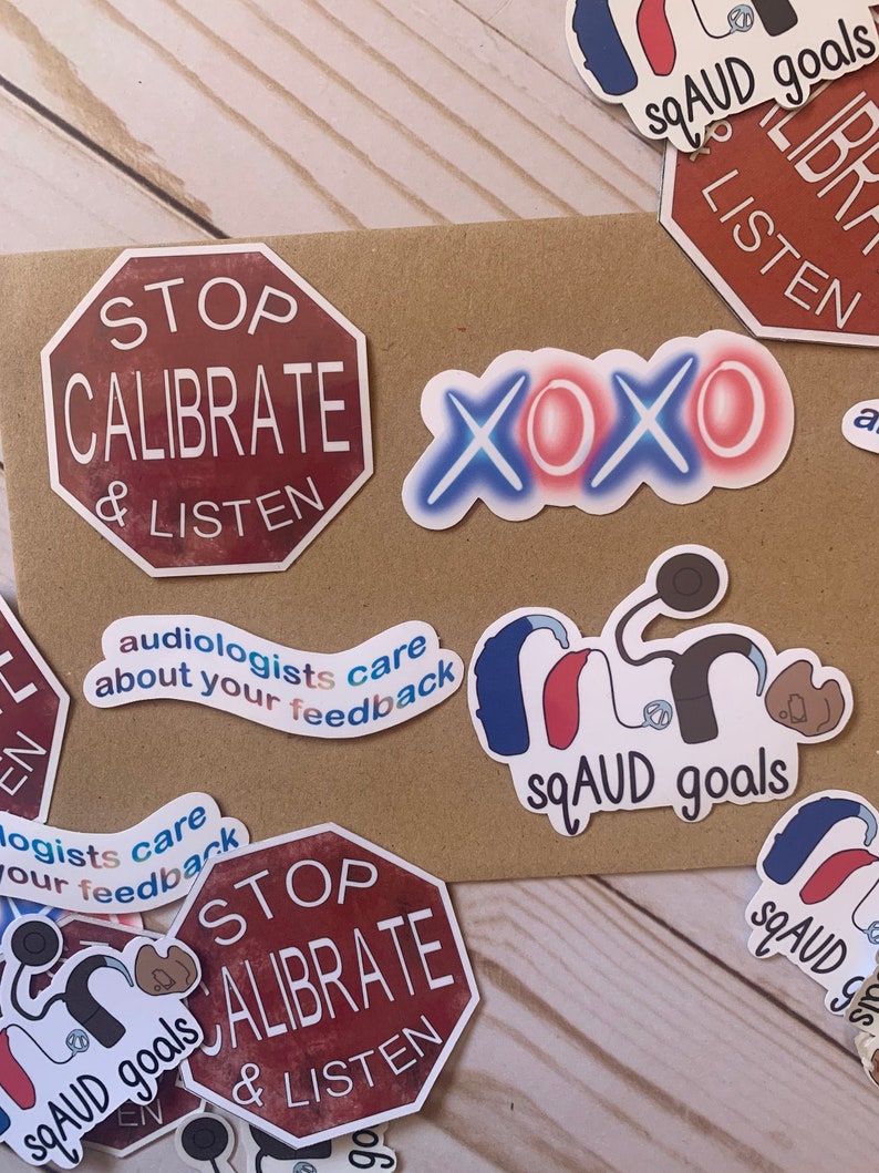 Op de afbeelding: Een verzameling stickers met verschillende ontwerpen, waaronder een stopteken met de tekst "STOP CALIBRATE & LISTEN", een hart met de tekst "XOXO", een hoortoestel met de tekst "sqAUD goals" en een sticker met de tekst "audiologists care about your feedback".