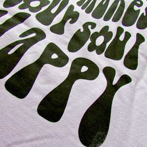 May include: A light purple t-shirt with a black graphic print that reads "Whatever makes your soul happy". The graphic is in a retro, psychedelic style.