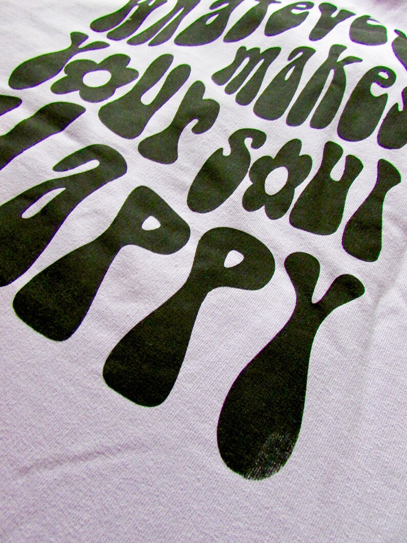May include: A light purple t-shirt with a black graphic print that reads "Whatever makes your soul happy". The graphic is in a retro, psychedelic style.