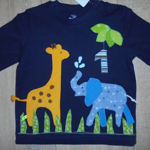 May include: A navy blue long-sleeved shirt with a giraffe, elephant, and palm tree applique. The shirt also has a number one with stripes and a green leaf design.