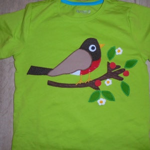 May include: A green t-shirt with an applique of a brown and red robin perched on a branch with green leaves and white flowers.