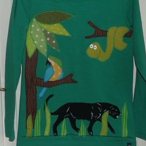May include: A green long-sleeved shirt with an embroidered jungle scene. The scene includes a black panther, a green snake, a blue and yellow parrot, and a brown tree with green leaves.