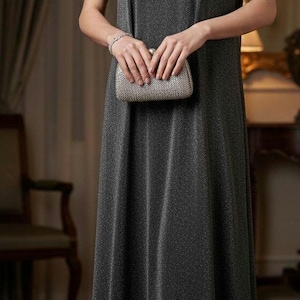 May include: A sleeveless, dark gray evening gown with a subtle shimmer. The dress is paired with a small, silver clutch. The neckline is embellished with small, dark beads. The overall look is elegant and formal.
