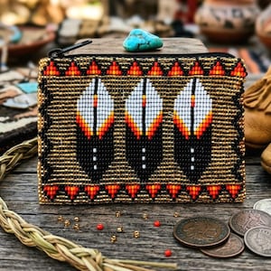 May include: A beaded coin purse with a black zipper, featuring a pattern of three stylized feathers in black, white, and orange. The purse is accented with gold beads and a turquoise stone. The design is reminiscent of Native American crafts.