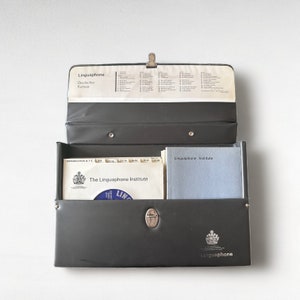 May include: A black leather carrying case with a silver clasp and the words "Linguaphone" and "The Linguaphone Institute" printed on it. The case is open and contains several vinyl records and a booklet.