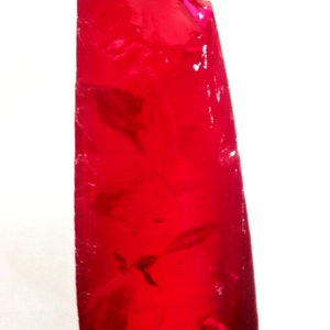 May include: A deep red, faceted gemstone with a rough, irregular shape. The gemstone is translucent and has a slight shimmer.