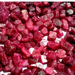 Könnte beinhalten: Eine Nahaufnahme eines Haufens loser, roher Rubingranate. Die Rubine sind tiefrot und haben verschiedene Formen und Größen.