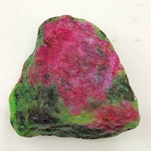 Peut inclure: Une pierre précieuse brute non polie avec un mélange de couleurs vertes, roses et noires. La pierre précieuse a une forme naturelle irrégulière.