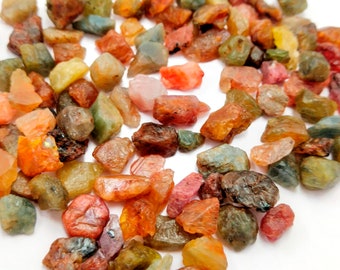 Könnte beinhalten: Eine Sammlung von bunten, rohen Edelsteinen, darunter Rot, Orange, Gelb, Grün und Blau. Die Edelsteine sind in verschiedenen Größen und Formen und auf einem weißen Hintergrund verstreut.