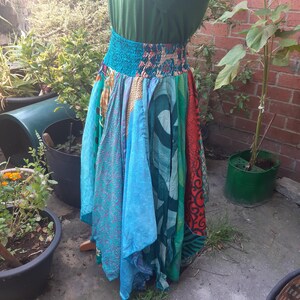 May include: A long, flowing skirt featuring a wide, smocked elastic waistband and a patchwork design composed of various fabric panels in shades of teal, turquoise, green, and red, with intricate patterns including floral and geometric motifs.