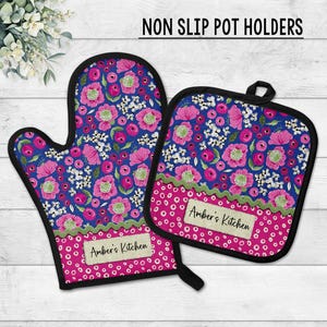 May include: A floral oven mitt and pot holder set. The blue background is covered with pink flowers and white accents. The bottom of each item is pink with white polka dots and the text "Amber's Kitchen". The set is trimmed in black.