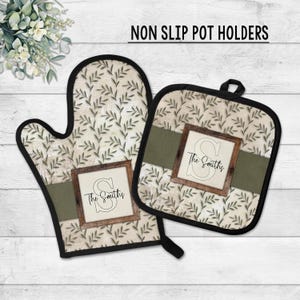 May include: A non-slip pot holder set featuring an oven mitt and a square pot holder. Both have a cream-colored background with a green leaf pattern. Each has a dark green band and a wooden-framed design with the text "The Smiths".