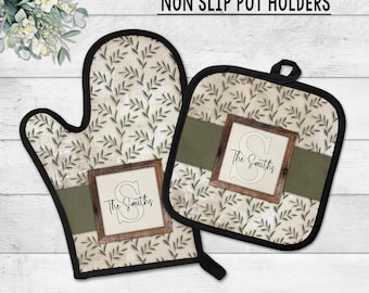 May include: A non-slip pot holder set featuring an oven mitt and a square pot holder. Both have a cream-colored background with a green leaf pattern. Each has a dark green band and a wooden-framed design with the text "The Smiths".