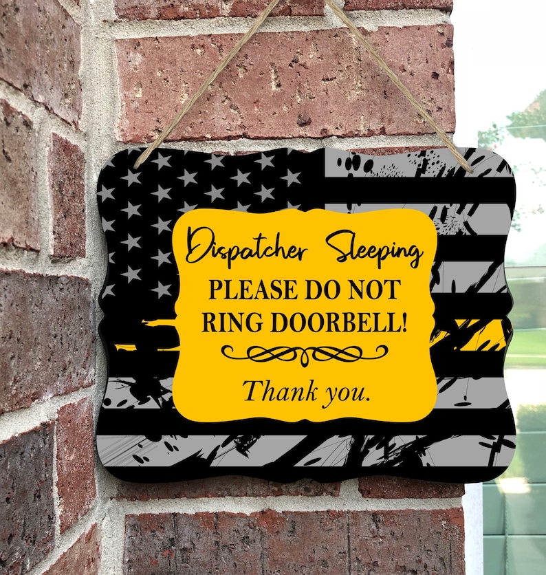 May include: A yellow and black sign with an American flag background. The sign reads "Dispatcher Sleeping Please Do Not Ring Doorbell! Thank you."