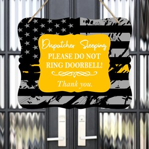 May include: A yellow sign with black and gray stripes and a thin yellow stripe across the top. The sign reads "Dispatcher Sleeping Please Do Not Ring Doorbell! Thank you."