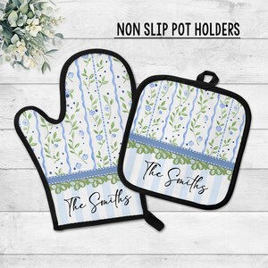 May include: A matching oven mitt and pot holder set. The white background features blue stripes and floral patterns. The set is trimmed in black and includes the text "The Smiths". The pot holder has a loop for hanging.