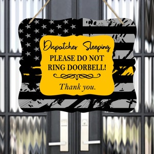 May include: A yellow and black sign with a thin yellow stripe across the top and the text "Dispatcher Sleeping Please Do Not Ring Doorbell! Thank you." on a yellow background.