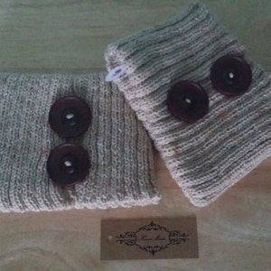 May include: A pair of beige knitted leg warmers with brown buttons. The leg warmers are made of a soft, cosy material and are perfect for keeping your legs warm in the winter.