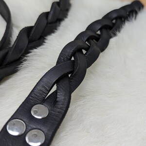 May include: Close-up of two black leather braided straps. One strap is in focus, showing a series of interwoven leather strands. The other strap is slightly out of focus. The focused strap has silver rivets.