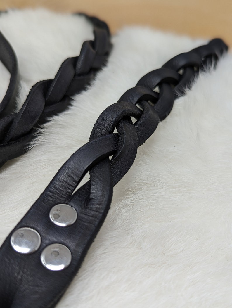 May include: Close-up of two black leather braided straps. One strap is in focus, showing a series of interwoven leather strands. The other strap is slightly out of focus. The focused strap has silver rivets.