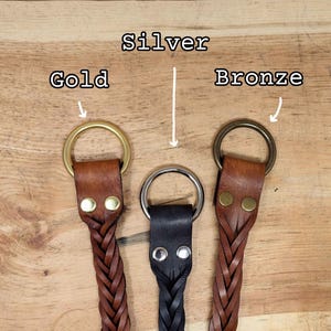 K&ouml;nnte beinhalten: Drei Leder-Schl&uuml;sselanh&auml;nger mit geflochtenen Riemen und Metallringen in Gold, Silber und Bronze. Das Leder ist braun und schwarz. Der Hintergrund ist eine Holzoberfl&auml;che. Die W&ouml;rter "Silver", "Gold" und "Bronze" sind dar&uuml;ber geschrieben.