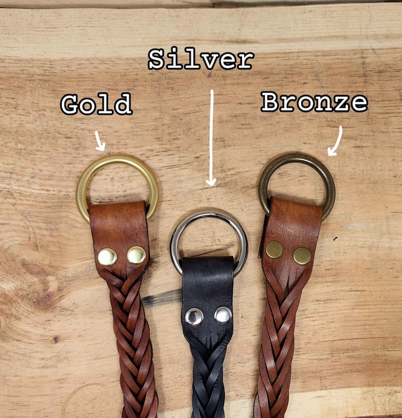 K&ouml;nnte beinhalten: Drei Leder-Schl&uuml;sselanh&auml;nger mit geflochtenen Riemen und Metallringen in Gold, Silber und Bronze. Das Leder ist braun und schwarz. Der Hintergrund ist eine Holzoberfl&auml;che. Die W&ouml;rter "Silver", "Gold" und "Bronze" sind dar&uuml;ber geschrieben.