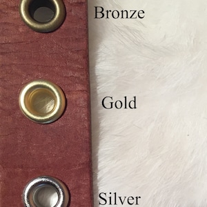 May include: Close-up of a burgundy leather strap with three metal grommets. The grommets are bronze, gold, and silver. The text "Bronze", "Gold", and "Silver" are next to each grommet.