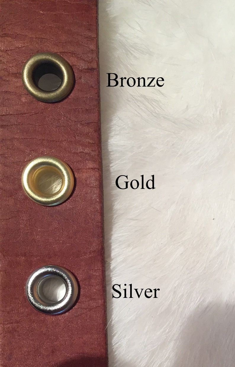 May include: Close-up of a burgundy leather strap with three metal grommets. The grommets are bronze, gold, and silver. The text "Bronze", "Gold", and "Silver" are next to each grommet.