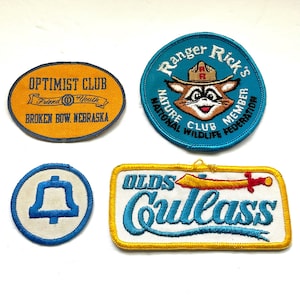 Może przedstawiać: Cztery, zabytkowe, haftowane naszywki. Jedna jest owalna z napisem "OPTIMIST CLUB". Kolejna jest okrągła z szopem i napisem "Ranger Rick's". Trzecia to niebieski dzwonek w okręgu. Ostatnia jest prostokątna z napisem "OLDS Cutlass".